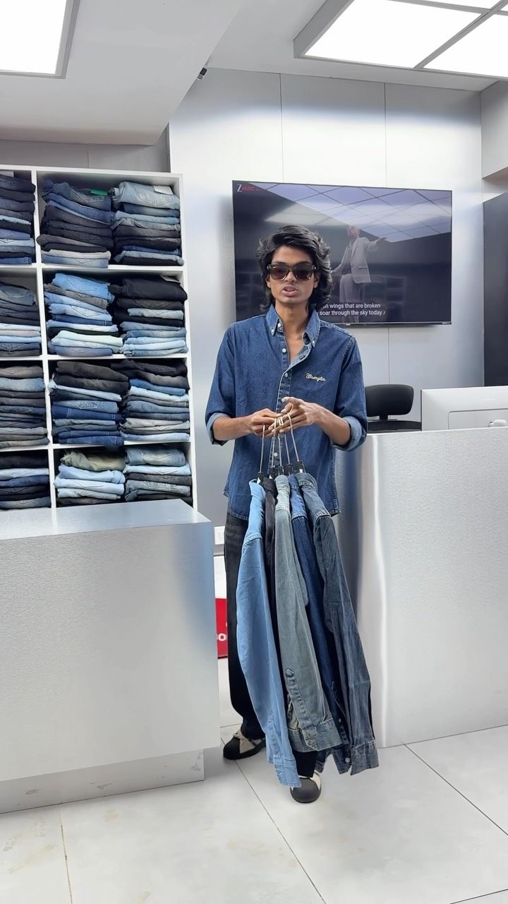 Model holding a stack of blue jeans in front of the denim shelves at Borntown