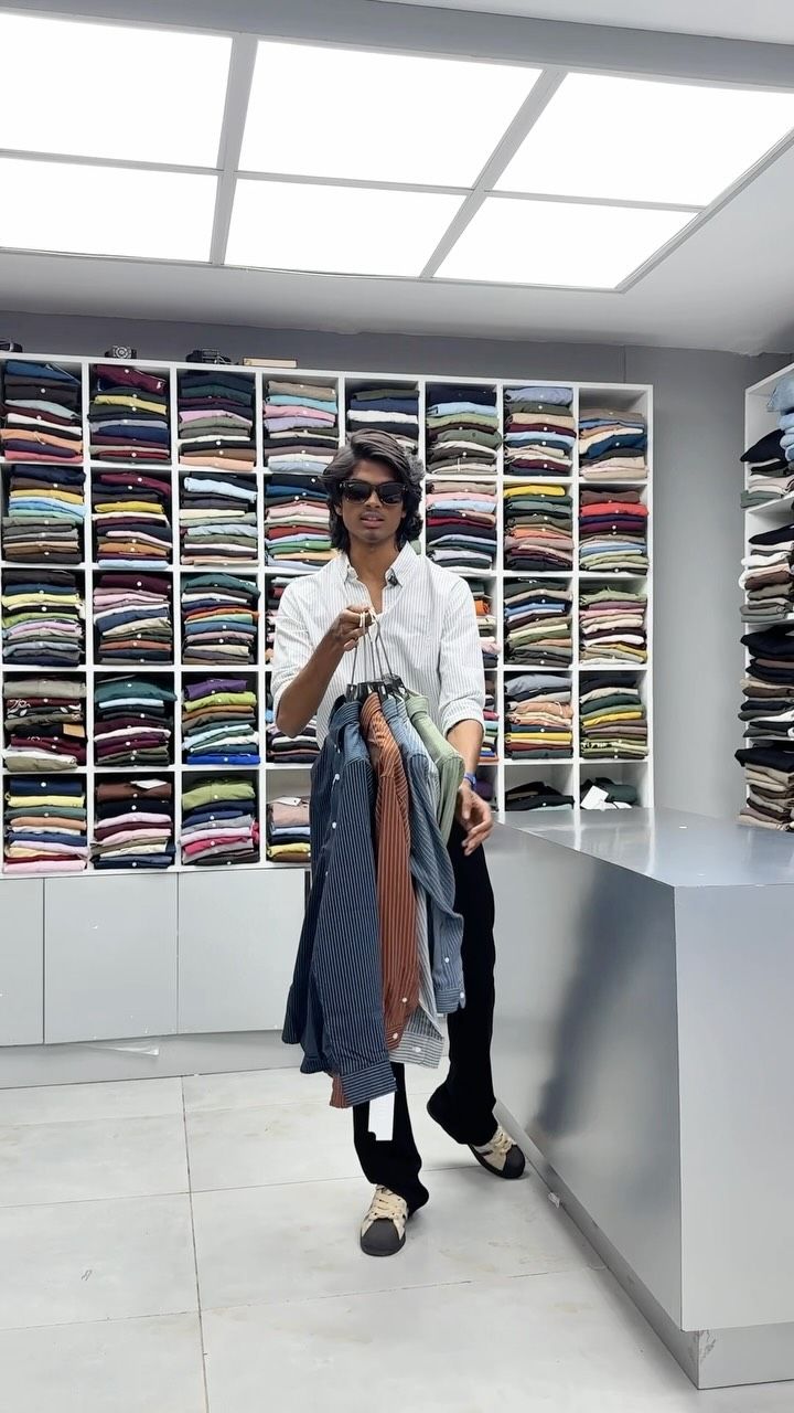 Model holding a stack of shirts in front of the shirt wall at Borntown
